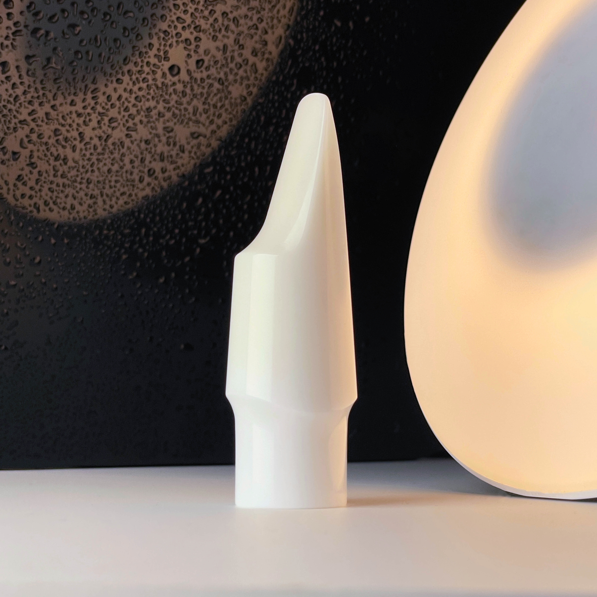Forme blanche incurvée en céramique technique posée sur un fond sombre texturé en gros plan